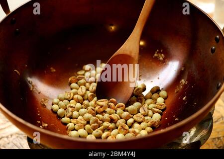 raw coffee beans being roasted in a brass pan with for Thai style home-brew coffee Stock Photo