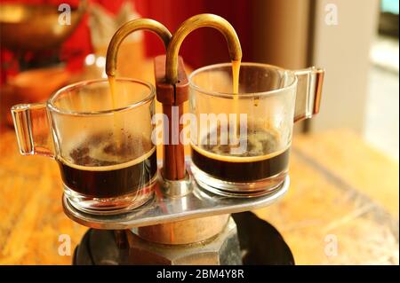 Espresso coffee trickling out from mini retro brewing pot into a pair of glass demitasse cups Stock Photo