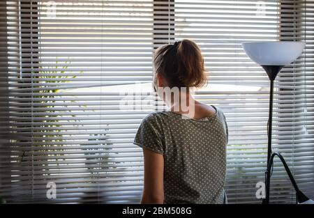 COVID-19 Quarantine mental health. Woman self isolated at home pensive looking out of window thinking of relationship, employment, coronavirus. Stock Photo