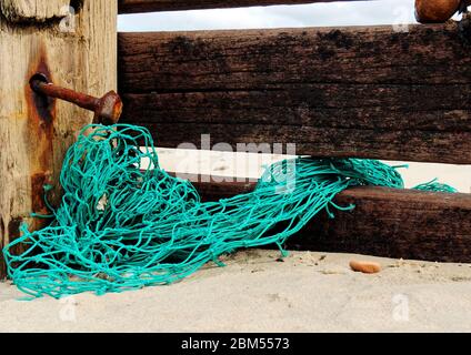 Torn nylon fishing net tangled round a wooden groyne on a beach
