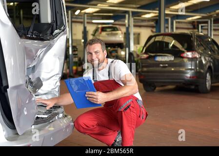Car mechanic examines accident vehicle in a workshop for repair Stock Photo