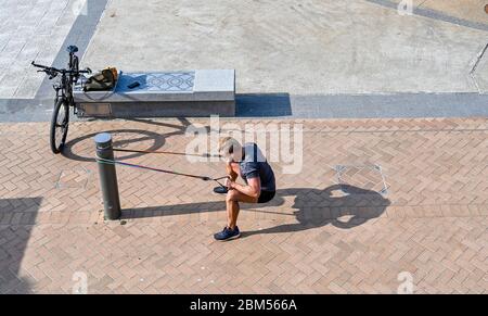 Brighton UK 7th May 2020 - Time for some physical stretches for this young man on Brighton seafront on a beautiful sunny morning during the Coronavirus COVID-19 pandemic crisis . The weather is forecast to be hot and sunny over the next few days before turning cooler at the weekend . Credit: Simon Dack / Alamy Live News Stock Photo