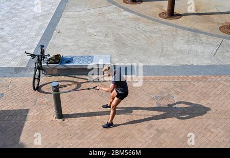 Brighton UK 7th May 2020 - Time for some physical stretches for this young man on Brighton seafront on a beautiful sunny morning during the Coronavirus COVID-19 pandemic crisis . The weather is forecast to be hot and sunny over the next few days before turning cooler at the weekend . Credit: Simon Dack / Alamy Live News Stock Photo