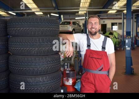 Portrait of successful smiling car mechanic in a workshop on a stack of tires at his workplace Stock Photo