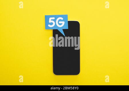 top view of speech bubble with 5g lettering near smartphone on yellow background Stock Photo