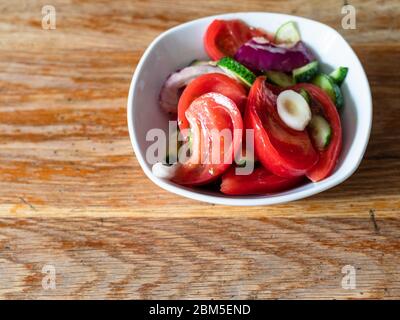 homemade vegetable salad from sliced fresh tomato, cucumber and onion in white bowl on shabby wooden table at home kitchen Stock Photo