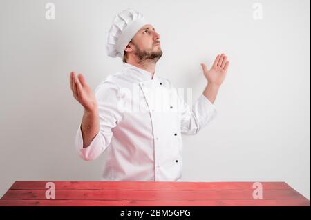 Portrait of young male chef in white uniform with open arms looking up, side view posing on a white isolated background Stock Photo
