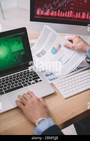Cropped view of data analyst using laptop and papers with graphs while testing security of computer systems Stock Photo