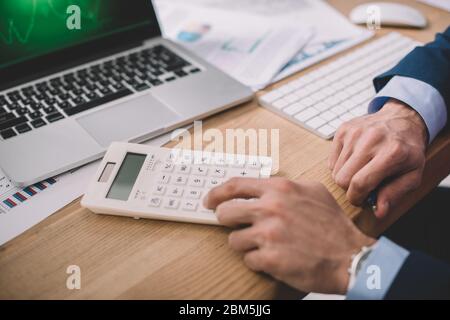 Cropped view of data analyst using calculator near laptop and papers on table Stock Photo