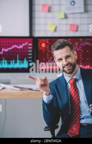Smiling information security analyst pointing with finger near computers on table in office Stock Photo