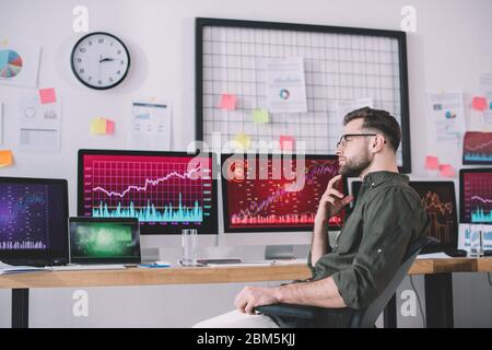 Side view of pensive data analyst looking away near charts on computer monitors in office Stock Photo