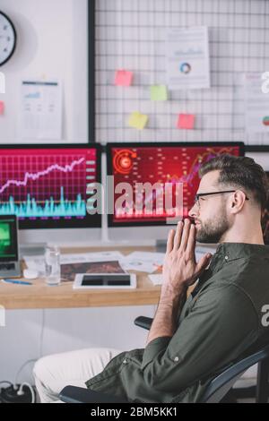 Side view of serious data analyst sitting at table with computers in office Stock Photo