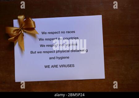 Warning sign about coronavirus printed on white paper with golden color bow placed on wooden surface, physical distancing concept Stock Photo