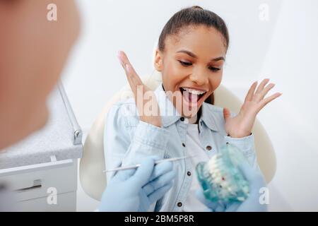 selective focus of excited african american woman in braces gesturing near dentist holding teeth model Stock Photo