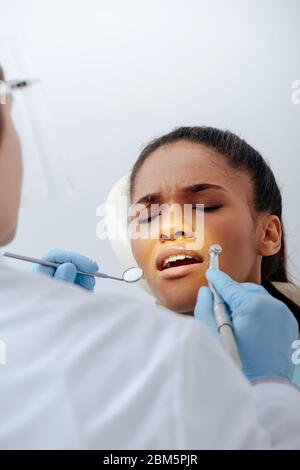 selective focus of orthodontist in latex gloves holding dental instruments near upset african american woman in braces Stock Photo
