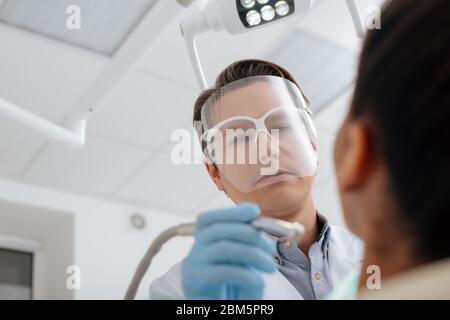 low angle view of dentist in face shield and latex gloves holding dental instrument near african american woman Stock Photo
