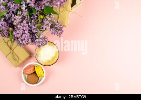 Cup of black coffee with milk and gift, lilac flowers and sweet pastel french macaroons on pink table. Top views with clear space Stock Photo