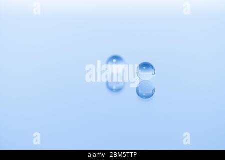 A marble in the foreground and a second marble is behind blurred, both reflected on a glossy, monochromatic blue image. Stock Photo
