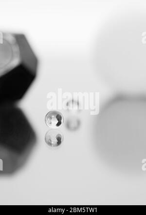 A marble in the foreground is reflected on a shiny shelf, in the background, you can see blurred a second marble and other geometric shapes, monochrome. Stock Photo