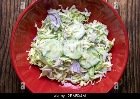 Fresh salad of autumn vegetables - green cabbage, cucumber, purple onions, parsley - in a red bowl on rustic wooden table. Rich and vitamin vegetarian Stock Photo