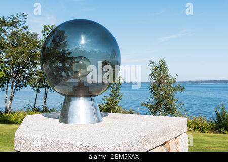 A glass orb with a light bulb inside and a view of Penobscot Bay with the sun and trees reflecting off of the glass. Stock Photo
