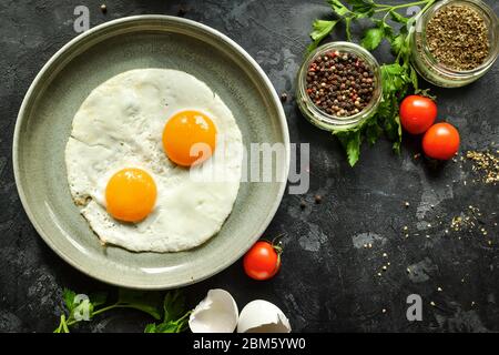 Fried eggs in a plate. Beautiful fried eggs. Tasty breakfast. Top view, dark concrete background. Stock Photo