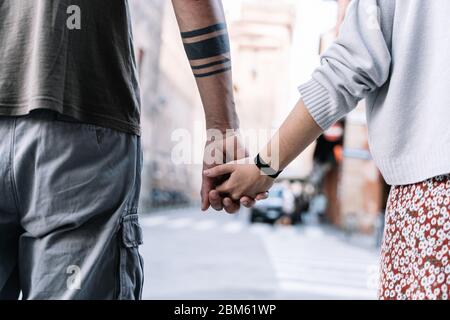 Detail of two young people with tattoos holding hands in the street Stock Photo