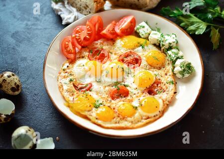 Fried quail eggs in a beautiful plate on a dark table background. Fried eggs with tomatoes and dill. Tasty and healthy breakfast. Stock Photo