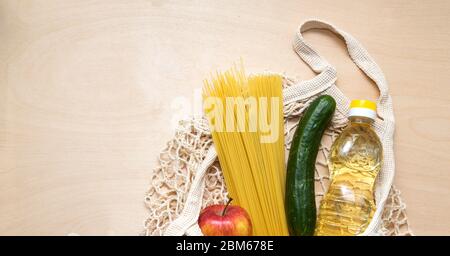 Food delivery. Eco bag net with food: oil, spaghetti, apple, cucumber for donations during quarantine. Food on the wood background Stock Photo