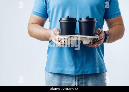 Man coffee shop worker giving takeaway cups of coffee on grey background Stock Photo