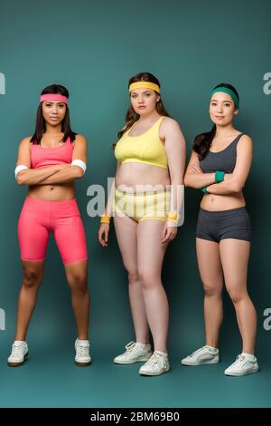 Multiethnic sportswomen with crossed arms looking at camera on green Stock Photo