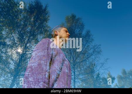 Double exposure of young handsome man and tall green trees overlaying against blue sky Stock Photo