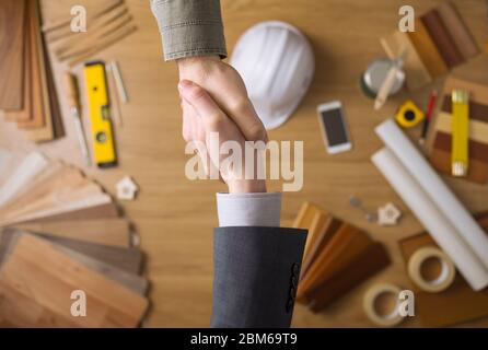 Construction engineer and businessman shaking hands top view close up, desktop with work tools and wood swatches on background Stock Photo