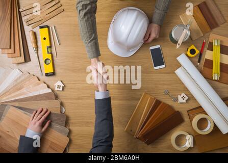 Construction engineer and businessman shaking hands top view close up, desktop with work tools and wood swatches on background Stock Photo