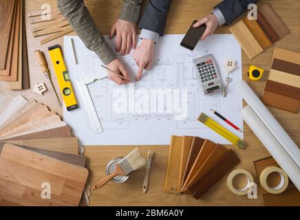 Business people working together on a building project, desktop top view with tools, wood swatches, mobile phone and blueprint Stock Photo