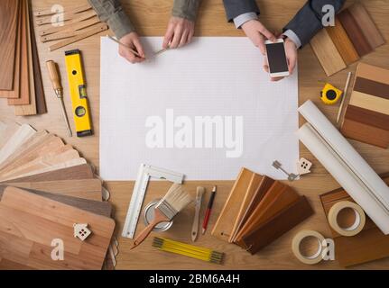 Construction engineer and businessman's hands working together at desk with blank blueprint project at center, work tools and wood swatches all around Stock Photo