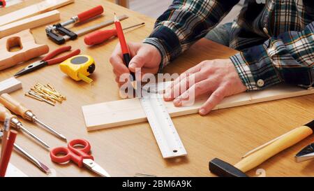 Man working on a DIY project and measuring a wooden plank with work tools all around, hands close up Stock Photo