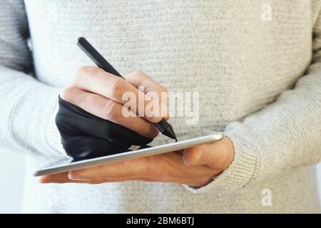 closeup of a caucasian man wearing a black two finger glove while is using a graphic pen in a digital tablet Stock Photo