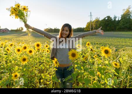 Happy young beautiful Asian woman holding flowers with open arms in the sunflower garden farm Stock Photo