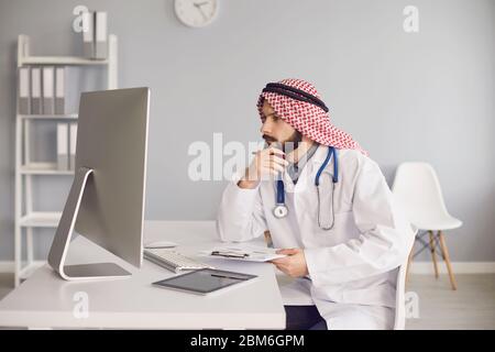 Arab male doctor working at a table with a computer in the office of a medical clinic. Stock Photo