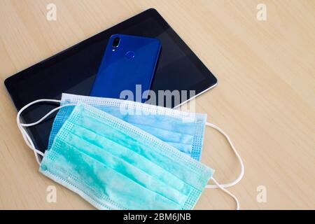 Blue and green mask lying on smartphone backside and digital tablet on table Stock Photo