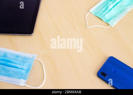 Blue and green mask smartphone and digital tablet lying in corners on wooden table Stock Photo