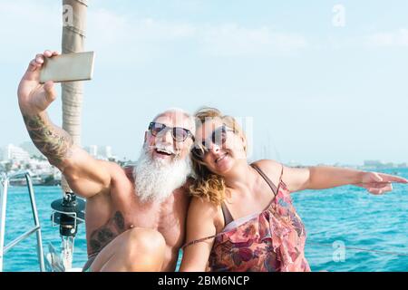 Senior couple taking selfie with mobile smartphone on sailboat vacation - Happy mature people having fun celebrating wedding anniversary on boat trip Stock Photo