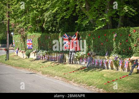 Ackworth, UK - May 07, 2020: A woman hitching Englands flag to green fence as a preparation to celebrate Victory in Europe in small village in West Yo Stock Photo