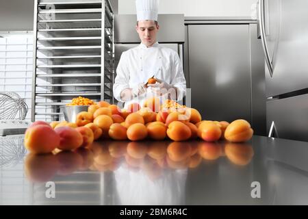 pastry chef at work in professional kitchen, makes apricot jam for the cake or for the croissants, on stainless steel worktop Stock Photo
