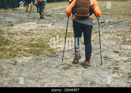 A group of people are hiking. In the foreground is an elderly woman with special Scandinavian poles. Stock Photo