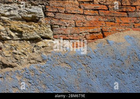 Old and weathered natural stone and brick wall with light blue paint plaster fallen off on on one side for background Stock Photo