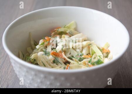 Healthy coleslaw salad with cabbage, carrots, dill and white dressing sauce in a white bowl on wooden surface Stock Photo
