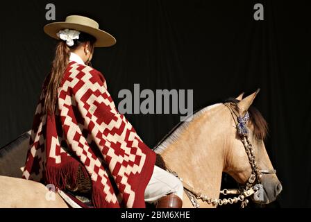 Argentinian woman wearing a traditional outfit riding a buckskin horse in the dark Stock Photo