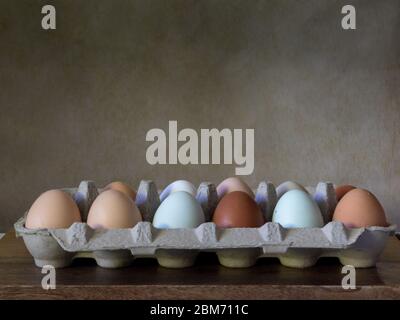 One dozen unwashed colorful chicken eggs in open cartonon on wooden surface viewed from the side and plenty of brown copy-space- free-range eggs of va Stock Photo